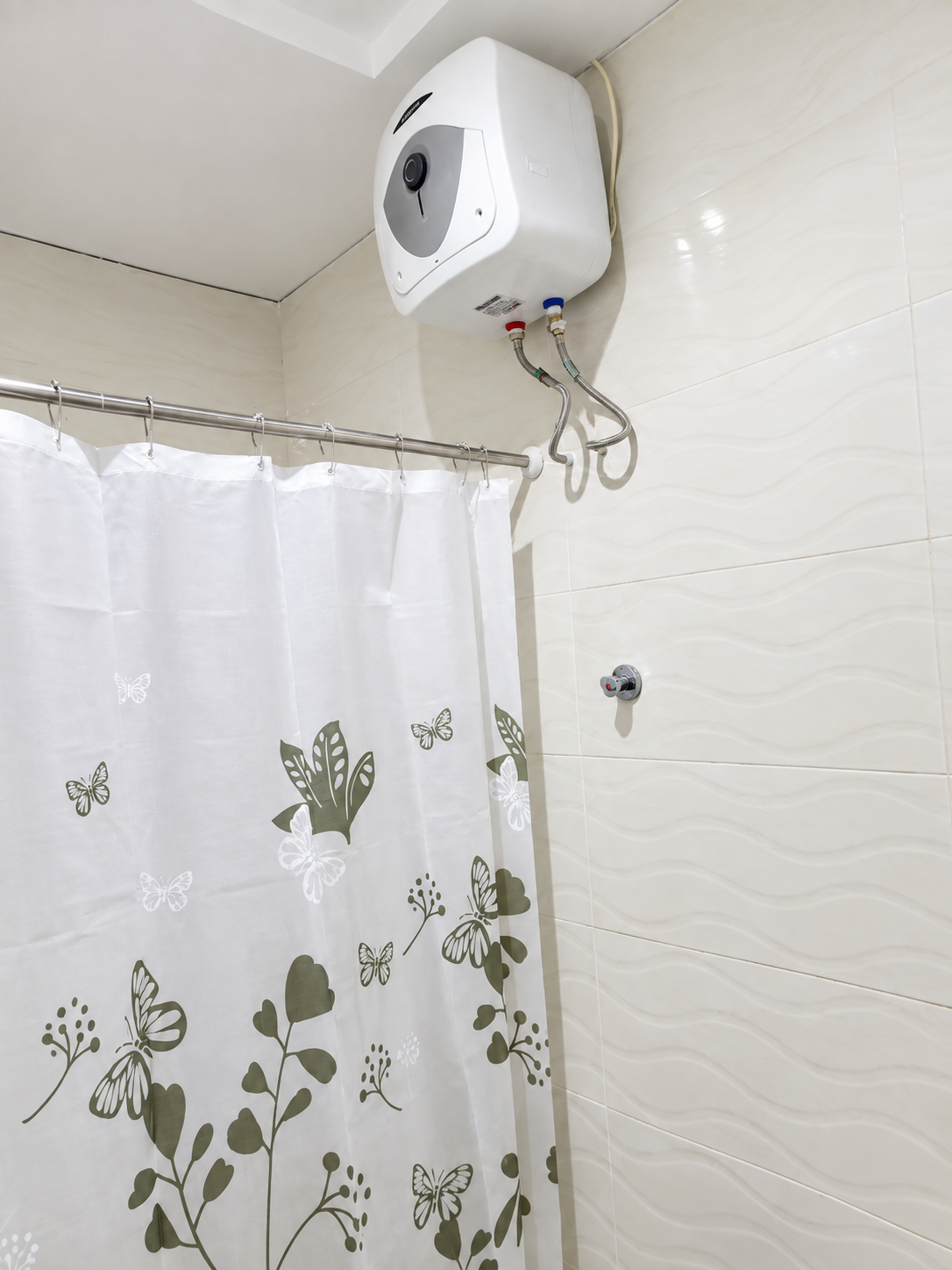 Tiled shower area with a wall-mounted water heater and patterned shower curtain