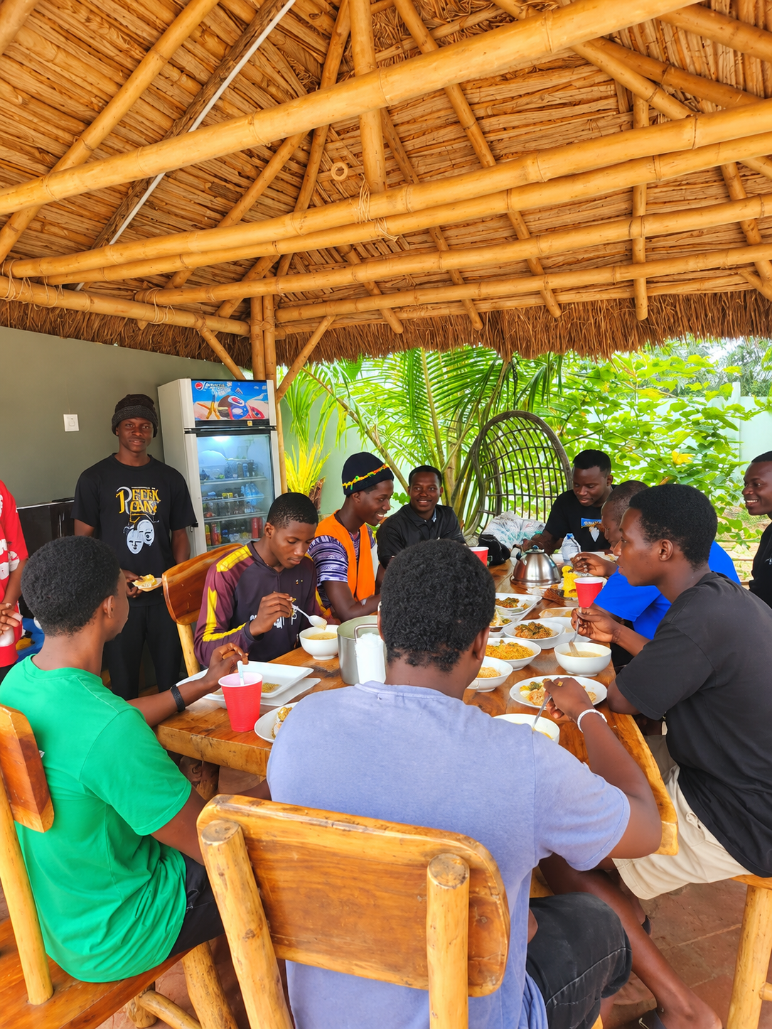 Guests sharing a meal around a table beneath a thatched bamboo pavilion